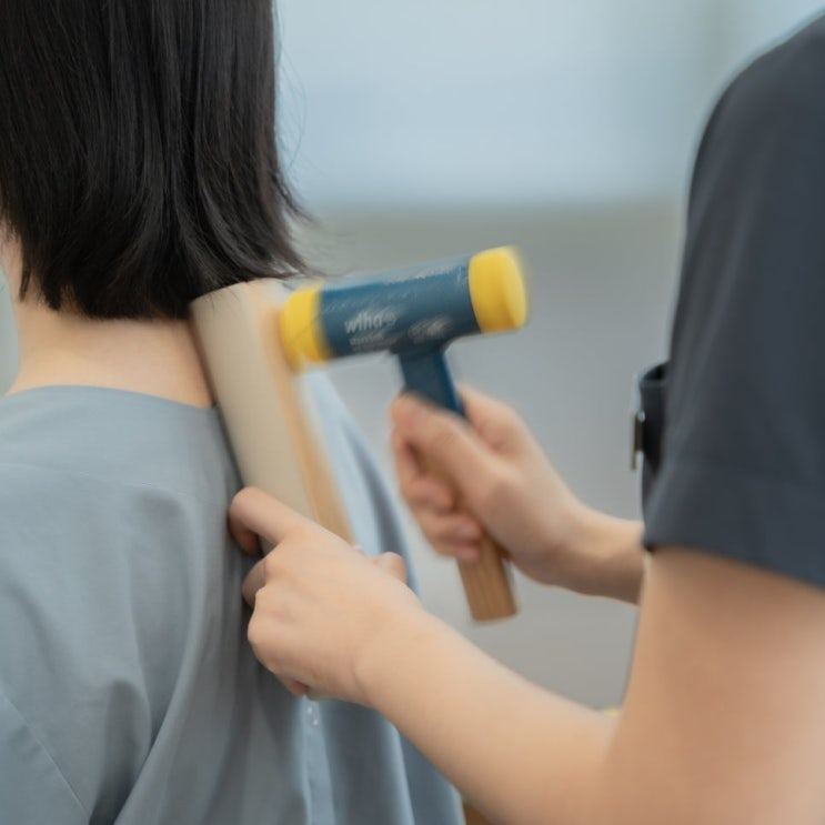 환자의 뒷목에 의료진이 타진 도구를 대는 치료 사진